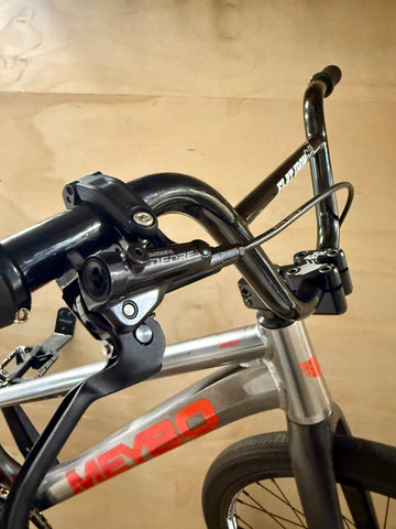 Close-up of a bicycle handlebar with brake lever against a beige wall.